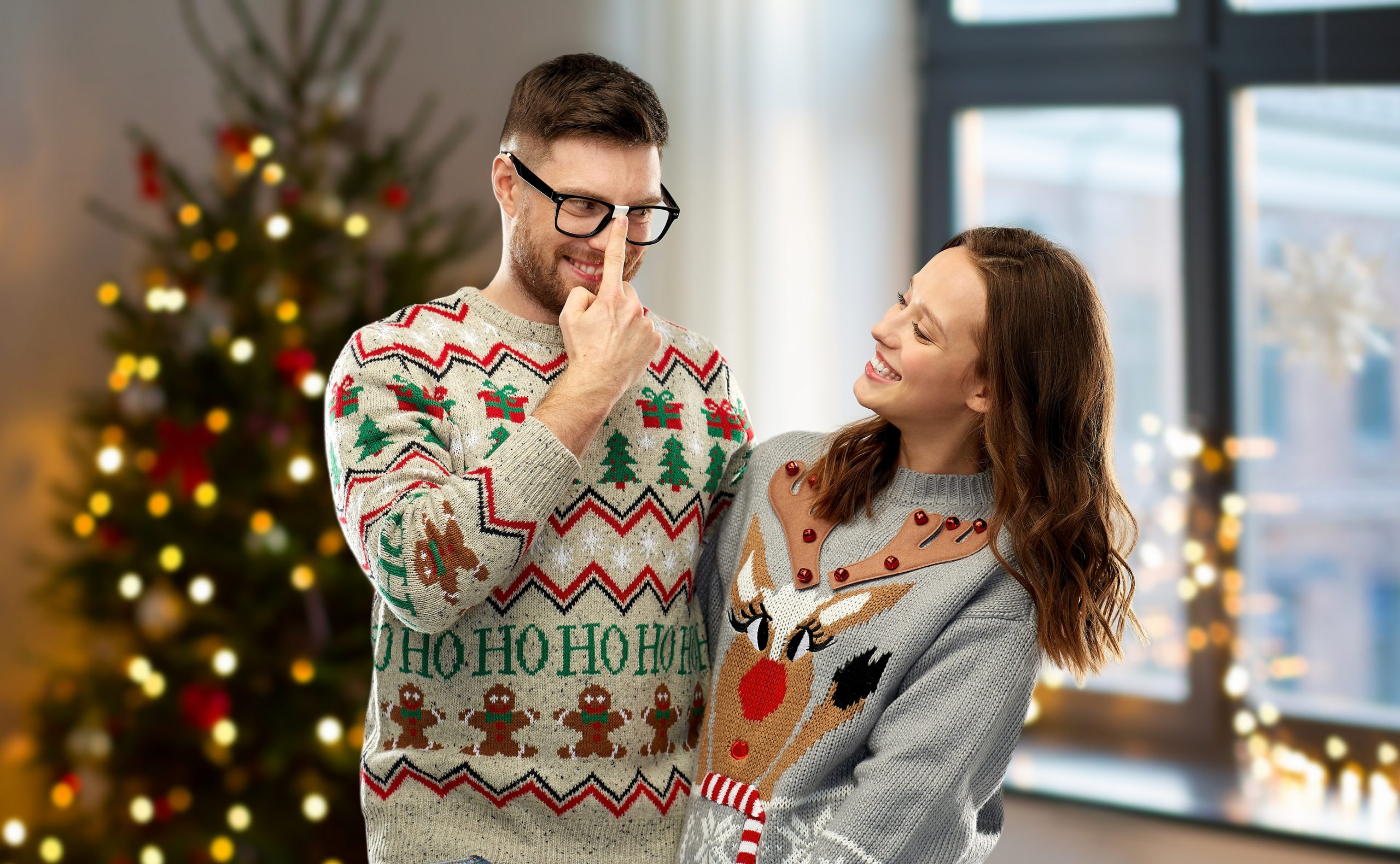man en vrouw in tweedehands foute kersttrui bij kerstboom